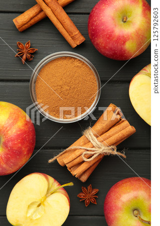 Red apple, cinnamon sticks and cinnamon in bowl on black wooden background. 125792603