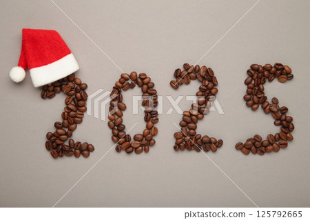 The inscription number 2025 laid out from coffee beans with Santa Claus hat. Happy New Year 2025 on grey background. Top view 125792665