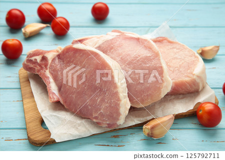 Sliced raw pork meat on cutting board on blue wooden background. Sliced raw pork meat on cutting board on blue wooden background. 125792711