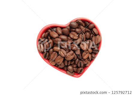 Coffee beans in the heart shaped bowl isolated on white background. Top view Coffee beans in the heart shaped bowl isolated on white background. Top view 125792712