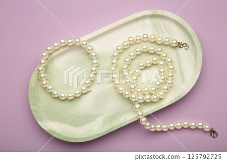 Elegant pearl necklace with bracelet on purple background, top view. Space for text Elegant pearl necklace with bracelet on purple background, top view. Space for text 125792725