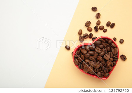 Coffee beans in the heart shaped bowl on light background. Top view Coffee beans in the heart shaped bowl on light background. Top view 125792760