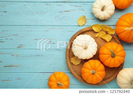 Autumn composition. Fresh orange and white pumpkin on wooden plate with autumn leaves on blue background. Top view 125792840