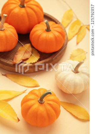 Autumn composition. Fresh orange and white pumpkin on wooden plate with autumn leaves on beige background. Autumn composition. Fresh orange and white pumpkin on wooden plate with autumn leaves on beige background. 125792857
