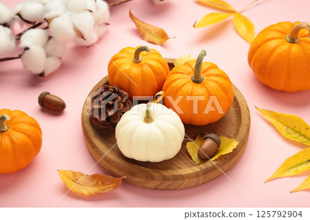 Autumn composition. Fresh orange and white pumpkin on wooden plate with autumn leaves on pink background. Top view Autumn composition. Fresh orange and white pumpkin on wooden plate with autumn leaves on pink background. Top view 125792904