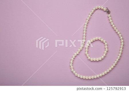Elegant pearl necklace with bracelet on purple background, top view. Space for text 125792913