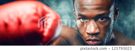 Boxer throwing punch in red gloves with intense expression on smoky background, close-up view. 125793023
