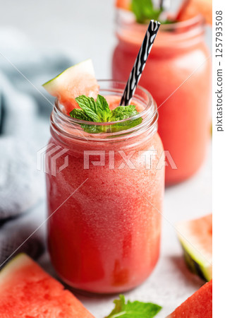 Refreshing watermelon smoothie in mason jar with mint leaves and striped straw on light background. 125793508