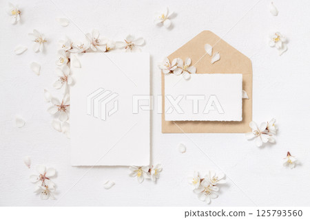 Blank cards and envelope near white cherry flowers top view, spring wedding mockup 125793560