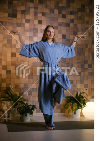 Girl in blue kimano practicing kundalini or qigong yoga in fitness gym . Spiritual energy, life force located at the base of the spine 125795523