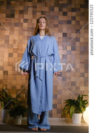 Girl in blue kimano practicing kundalini or qigong yoga in fitness gym . Spiritual energy, life force located at the base of the spine Girl in blue kimano practicing kundalini or qigong yoga in fitness gym . Spiritual energy, life force located at the base of the spine 125795525