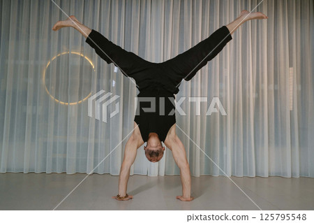 A man stands on his hands in the gym. Athletic man performs arm strength exercise in the gym A man stands on his hands in the gym. Athletic man performs arm strength exercise in the gym 125795548