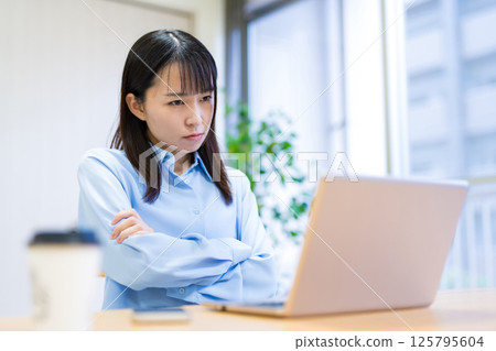 A woman thinking while looking at a computer and folding her arms 125795604