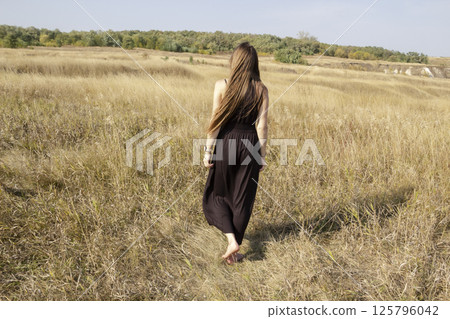 Pretty young dark haired woman in black dress stand in field. Beautiful girl outdoor in the field enjoy with freedom Pretty young dark haired woman in black dress stand in field. Beautiful girl outdoor in the field enjoy with freedom 125796042