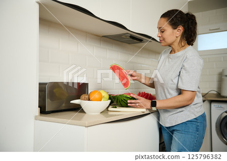 Woman Preparing Fresh Watermelon Slices in a Modern Kitchen Interior 125796382