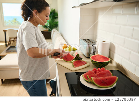 Woman Preparing Fresh Watermelon Slices in a Modern Kitchen Setting 125796387