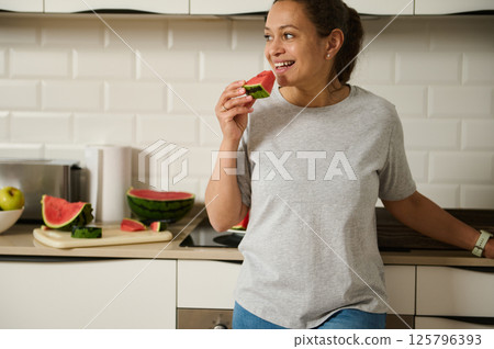 Smiling Woman Enjoying Fresh Watermelon in a Modern Kitchen Setting 125796393