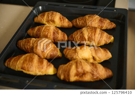 Freshly Baked Golden Croissants on a Baking Tray in a Cozy Kitchen Setting Freshly Baked Golden Croissants on a Baking Tray in a Cozy Kitchen Setting 125796410