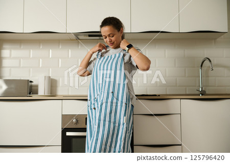 Woman Adjusting Apron in a Modern, Minimalistic Kitchen Setting Woman Adjusting Apron in a Modern, Minimalistic Kitchen Setting 125796420