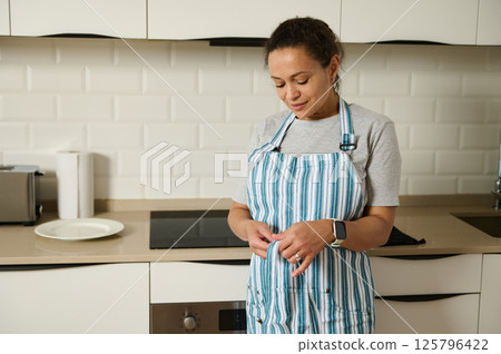 Woman in a Kitchen Preparing Meal Wearing Striped Apron Woman in a Kitchen Preparing Meal Wearing Striped Apron 125796422