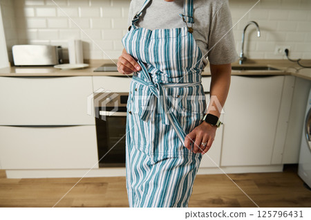 Person Adjusting a Striped Apron in a Modern Kitchen Setting Person Adjusting a Striped Apron in a Modern Kitchen Setting 125796431