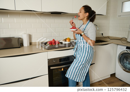 Woman Enjoying Fresh Watermelon in a Modern Kitchen Setting Woman Enjoying Fresh Watermelon in a Modern Kitchen Setting 125796432