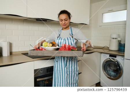 Woman Carrying Tray of Fresh Fruits in a Cozy Domestic Kitchen 125796439