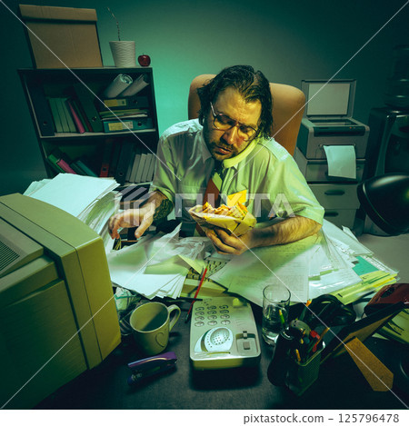 Exhausted office man eats sandwich, buried in papers on messy desk, symbolizing corporate burnout, multitasking, overload, stress management. Exhausted office man eats sandwich, buried in papers on messy desk, symbolizing corporate burnout, multitasking, overload, stress management. 125796478