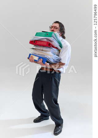 Office worker holding huge stack of binders and documents, being completely buried and overwhelmed by endless paperwork. Office worker holding huge stack of binders and documents, being completely buried and overwhelmed by endless paperwork. 125796499