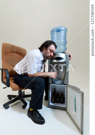 Exhausted office worker with glasses slumps against water cooler, eyes closed, showing signs of severe burnout and need for break. Exhausted office worker with glasses slumps against water cooler, eyes closed, showing signs of severe burnout and need for break. 125796504