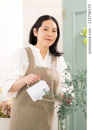 Smiling adult woman watering plants indoors | Flower shop gardening shop classroom image | Well-being girl | Well-being 125796574