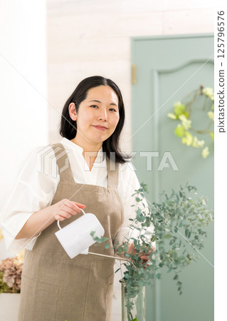 微笑的成年女性在室內澆灌植物 |花店園藝店教室圖片|幸福女孩 |福利 125796576