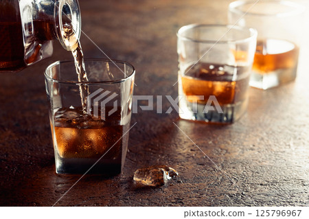 Pouring whiskey into a glass with ice. Pouring whiskey into a glass with ice. 125796967