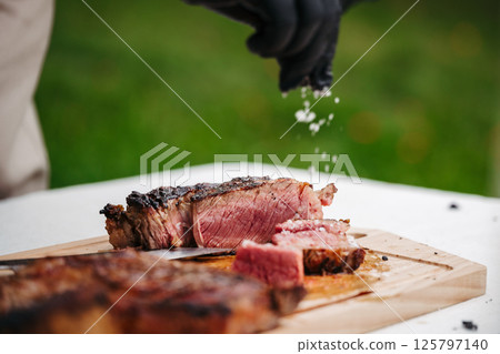 Chef salting juicy grilled steak on wooden cutting board. Chef salting juicy grilled steak on wooden cutting board. 125797140