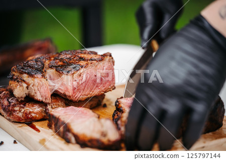 Chef slicing juicy grilled steak on wooden cutting board. Chef slicing juicy grilled steak on wooden cutting board. 125797144