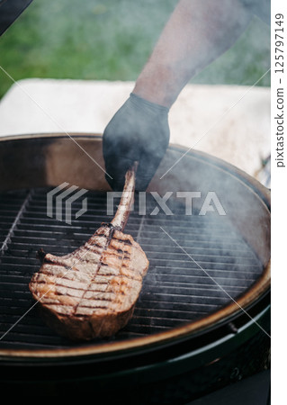 Grilling juicy Tomahawk steak on barbecue grill with smoke rising. Grilling juicy Tomahawk steak on barbecue grill with smoke rising. 125797149