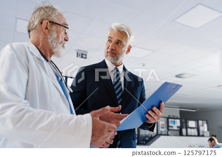 Doctor talking with hospital manager, walking down hospital hallway. 125797175