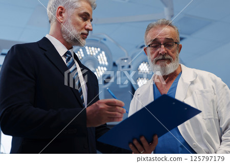 Doctor talking with hospital manager, standing in examination room. Doctor talking with hospital manager, standing in examination room. 125797179