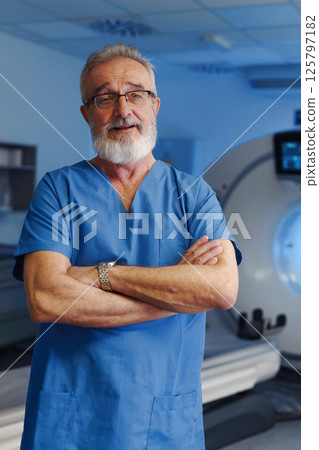 Medical specialist standing by CT scanner, looking at camera, hospital setting. Medical specialist standing by CT scanner, looking at camera, hospital setting. 125797182