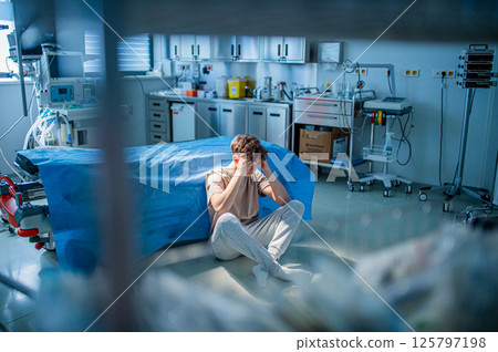 Worried teenage patient sitting alone on hospital floor, struggling with mental health issues. 125797198