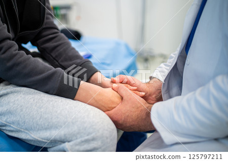 Close up of compassionate doctor holding hands of anxious teenage patient before surgery. 125797211