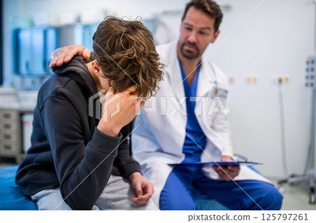 Depressed teenage patient sitting on hospital bed, talking with caring doctor. 125797261