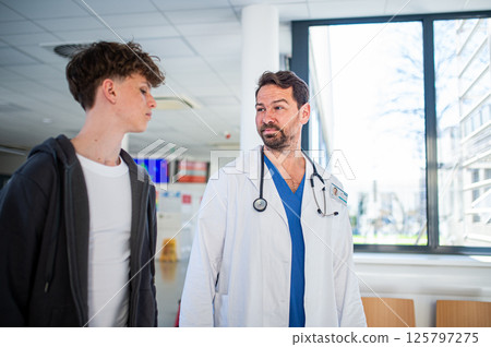 Doctor walking with teenage patient after successful medical procedure in hospital. 125797275