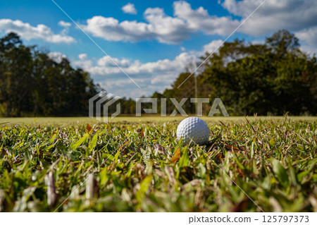 Golf ball on green grass in the evening golf course with sunshine background. Golf ball on green grass in the evening golf course with sunshine background. 125797373