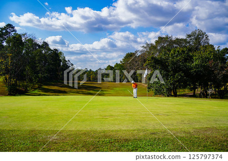 Golfer playing golf in the evening golf course, on sun set evening time. 125797374