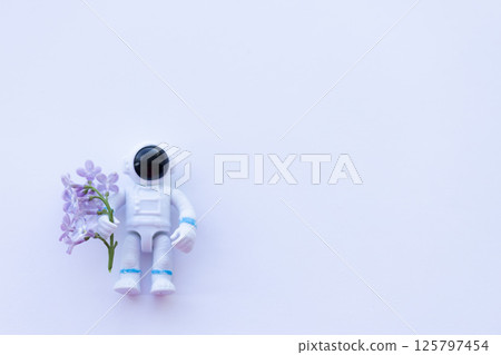 A toy spaceman holding lilac flowers. On a white background , copy space. 125797454