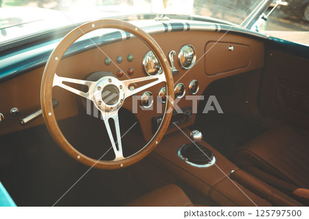 Vintage classic car interior featuring leather seats, chrome gauges, wooden steering wheel and polished dashboard Vintage classic car interior featuring leather seats, chrome gauges, wooden steering wheel and polished dashboard 125797500