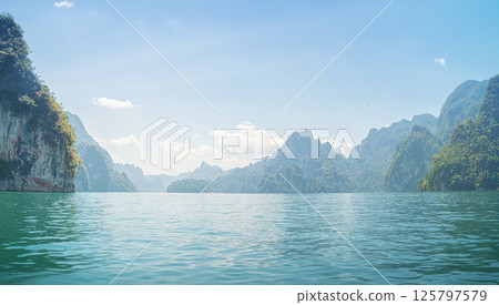 Majestic Cheow Lan Lake landscape showcases tranquil waters surrounded by lush mountains and clear skies in Thailand 125797579