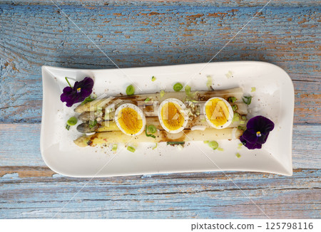 Baked asparagus with boiled egg in big white plate on blue background 125798116