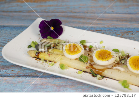 Baked asparagus with boiled egg in big white plate on blue background 125798117